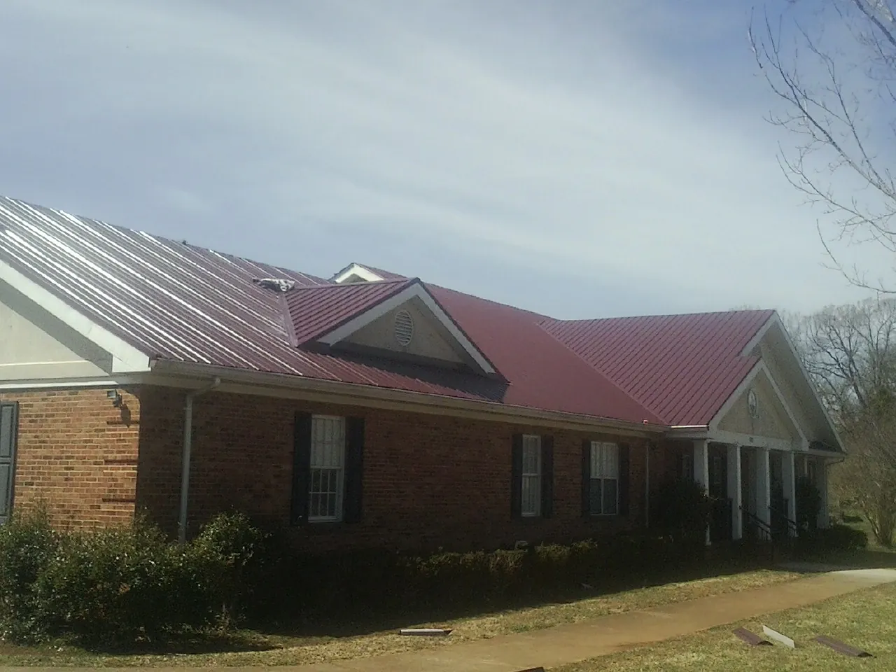 Red metal roof with gabled entries on a long brick building, from a Hail Damage Roof Repair job in Conway